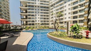 A swimming pool with blue mosaic tiles, surrounded by lounge chairs and plants, with high-rise buildings in the background. - Gorgeous 2BR Apartment at Gateway Pasteur near Exit Toll (Cimahi)