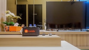 Un mostrador de recepción con un cartel de 'Travelio', un televisor de pantalla plana grande y una planta en maceta.