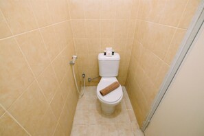 Une petite salle de bain carrelée, avec des toilettes, une serviette posée sur la lunette et un porte-rouleau de papier toilette.