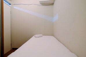 Une petite pièce étroite, avec un lit simple et une serviette enroulée posée dessus.