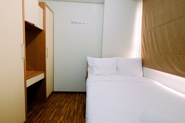 Une petite chambre à coucher, bien rangée, avec une armoire en bois, un lit avec une literie blanche et un mur de couleur claire.