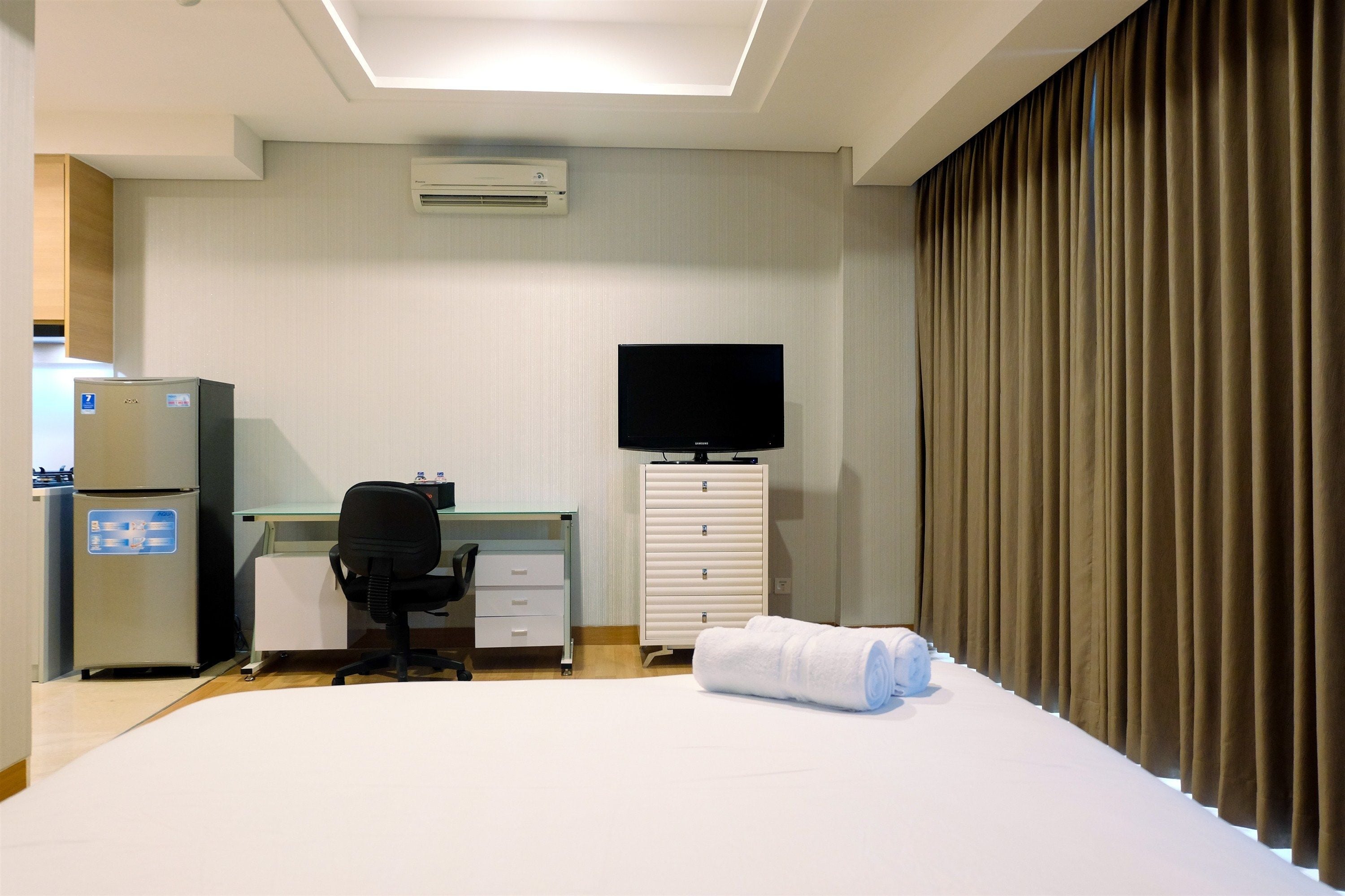 A hotel room with a bed, a desk, a chair, a television, a wardrobe, and an air conditioning unit.