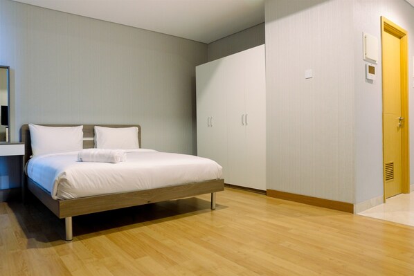 A modern bedroom with a wooden bed, white bedding, a wardrobe, and a door.