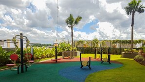 An outdoor exercise area with various fitness equipment, surrounded by green grass and palm trees. - Minimalist 2BR Apartment at M-Town Residence (Gading Serpong)
