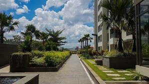 A pathway lined with planters and palm trees, leading to a modern building with large windows. - Minimalist 2BR Apartment at M-Town Residence (Gading Serpong)