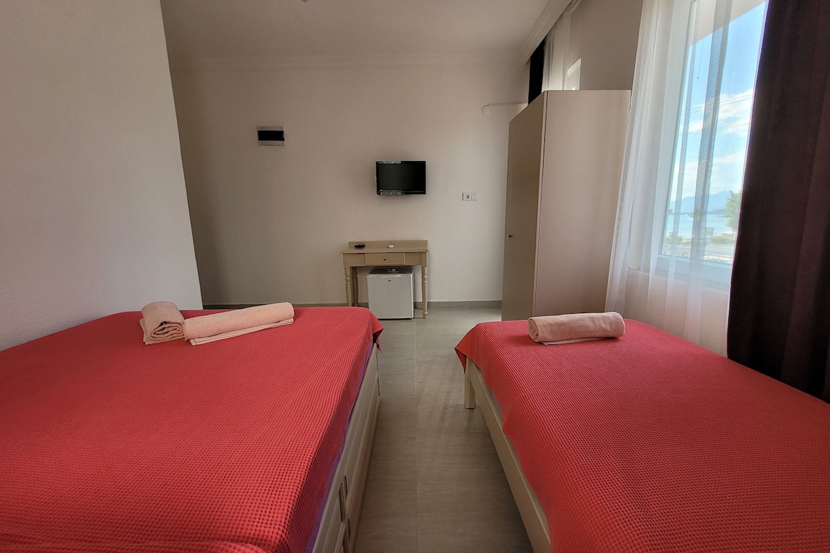 A hotel room with two beds, a desk, a television, and a window with a view.