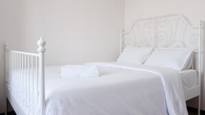 Un letto in metallo bianco con testiera, biancheria da letto bianca e un solo cuscino bianco.