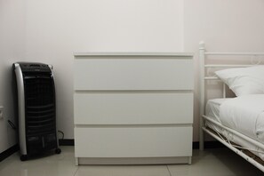 En vit säng med en metallram, ett vitt sängbord och en vit byrå med lådor.