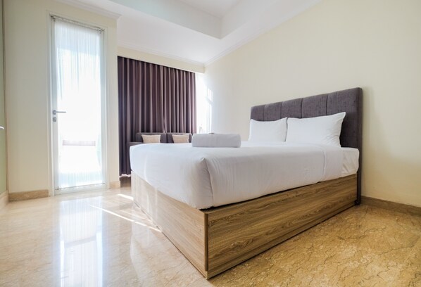 A modern hotel room with a large bed, a wooden headboard, and a view of the outdoors through a sliding door.
