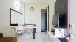 A modern hotel room with a flat-screen TV, a dining table with chairs, a sofa, and a large mirror.