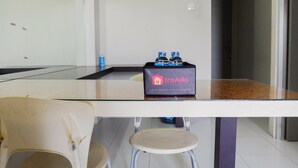 A small kitchenette area with a glass-top table, a white chair, and a stool. There is a box labeled 'Travello' with two bottles on top.