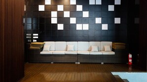 Moderni sisustus, jossa on tumma seinä, jossa on valkoisista neliöistä muodostuva geometrinen kuvio, vaaleanvärinen sohva tyynyineen ja puulattia.