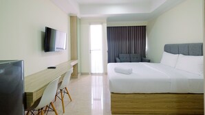 A hotel room with a bed, a desk with a chair, a television, and a window with curtains. - Simply Modern Studio Menteng Park Apartment (Jakarta)