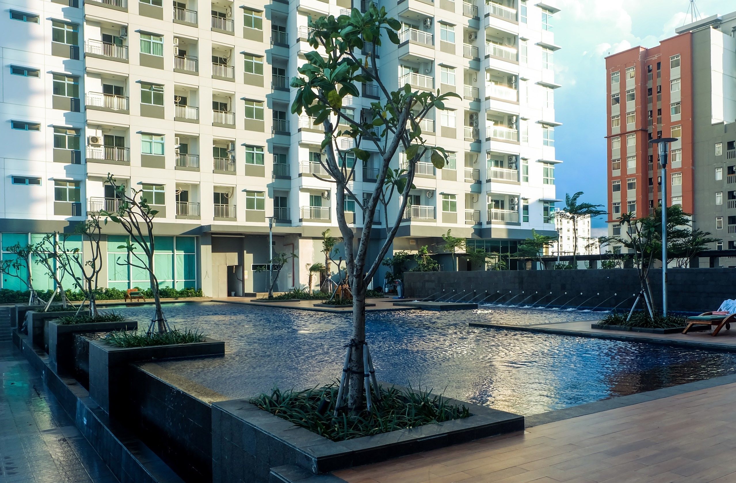 A modern building with multiple balconies, a central water feature, and a well-maintained garden area.