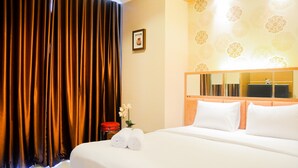 Una habitación de hotel con una cama grande, cabecera con espejo, mesita de noche roja y una cortina.
