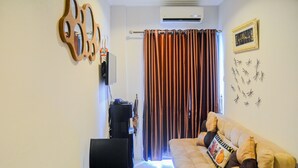 Una sala de estar con un sofá color beige, un televisor, un espejo montado en la pared y una cortina.
