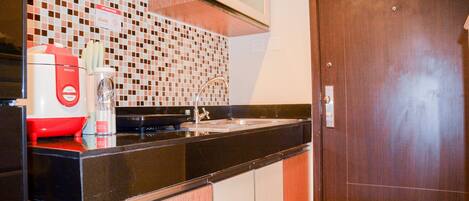 A compact kitchen with a black countertop, a red coffee maker, a microwave, and a tiled backsplash.