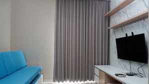 A modern living room with a blue sofa, a grey curtain, a white TV stand, and a marble wall. - Strategic 1BR Apartment at Ciputra International (Jakarta)