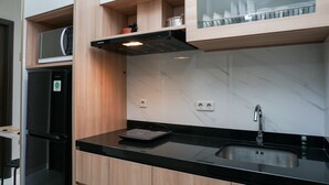 A modern kitchen with a black countertop, a stainless steel sink, and wooden cabinets. - Strategic 1BR Apartment at Ciputra International (Jakarta)