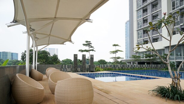 A rooftop pool area with lounge chairs and a large umbrella. - Strategic 1BR Apartment at Ciputra International (Jakarta)