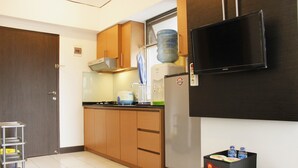 A compact kitchen with wooden cabinets, a stainless steel refrigerator, a water dispenser, and a flat-screen TV mounted on the wall. - Strategic 1BR Apartment with Sofa Bed at The Jarrdin Cihampelas (Bandung)