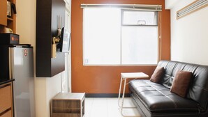 A compact living space with a black leather sofa, a small white table, and a kitchenette area with a refrigerator and microwave. - Strategic 1BR Apartment with Sofa Bed at The Jarrdin Cihampelas (Bandung)