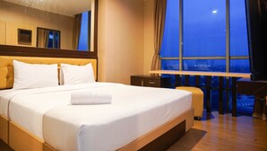 Habitación de hotel con una cama grande, un escritorio y vistas de la ciudad de noche.