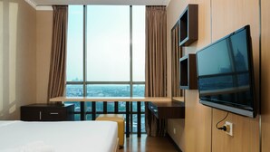 Una habitación de hotel con una cama grande, un escritorio, un televisor y vistas de la ciudad a través de amplios ventanales.