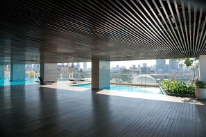 A spacious indoor area with a pool, lounge chairs, and a view of the city skyline.