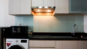 Ett kompakt kök med inbyggd mikrovågsugn, tvättmaskin och en diskho i rostfritt stål.