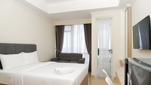 Ett hotellrum med en stor säng, en grå soffa, en tv och en dörr som leder ut till en balkong.