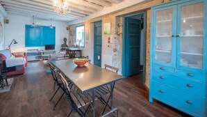 Un comedor con una mesa larga, sillas y una araña. Hay una cocina con armarios azules y una pared de piedra.