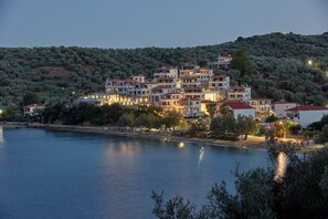 A coastal town with multi-story buildings, a waterfront, and a hillside with dense vegetation. - Olivia Sports and Sea (Almyros)