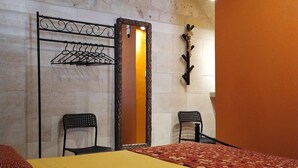 Una habitación con cama, dos sillas, perchero y puerta con espejo.
