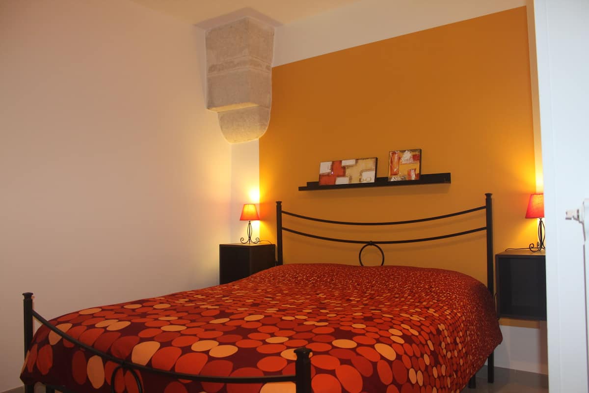 A bed with a patterned bedspread, two bedside lamps, a shelf with items, and a stone accent on the wall.
