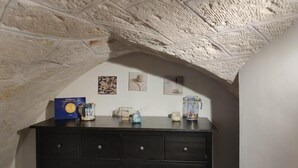 Un rincón de paredes de piedra con un aparador de madera oscura. Sobre el aparador, hay objetos decorativos, una caja azul y un recipiente de vidrio.