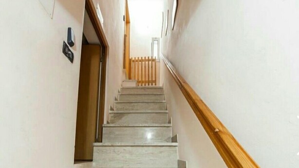 Una escalera con escalones de mármol y barandillas de madera, que conduce a un rellano con una puerta.
