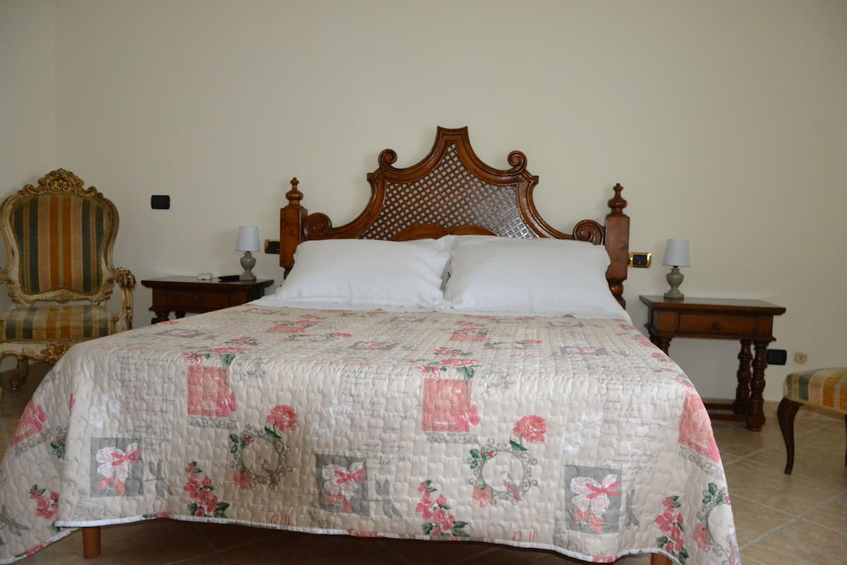 A bed with a floral quilt, a wooden headboard, two bedside tables with lamps, and a striped armchair.