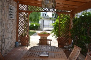 A wooden pergola with a table and chairs, surrounded by potted plants and a stone wall. - Villa Lucia (Bari)