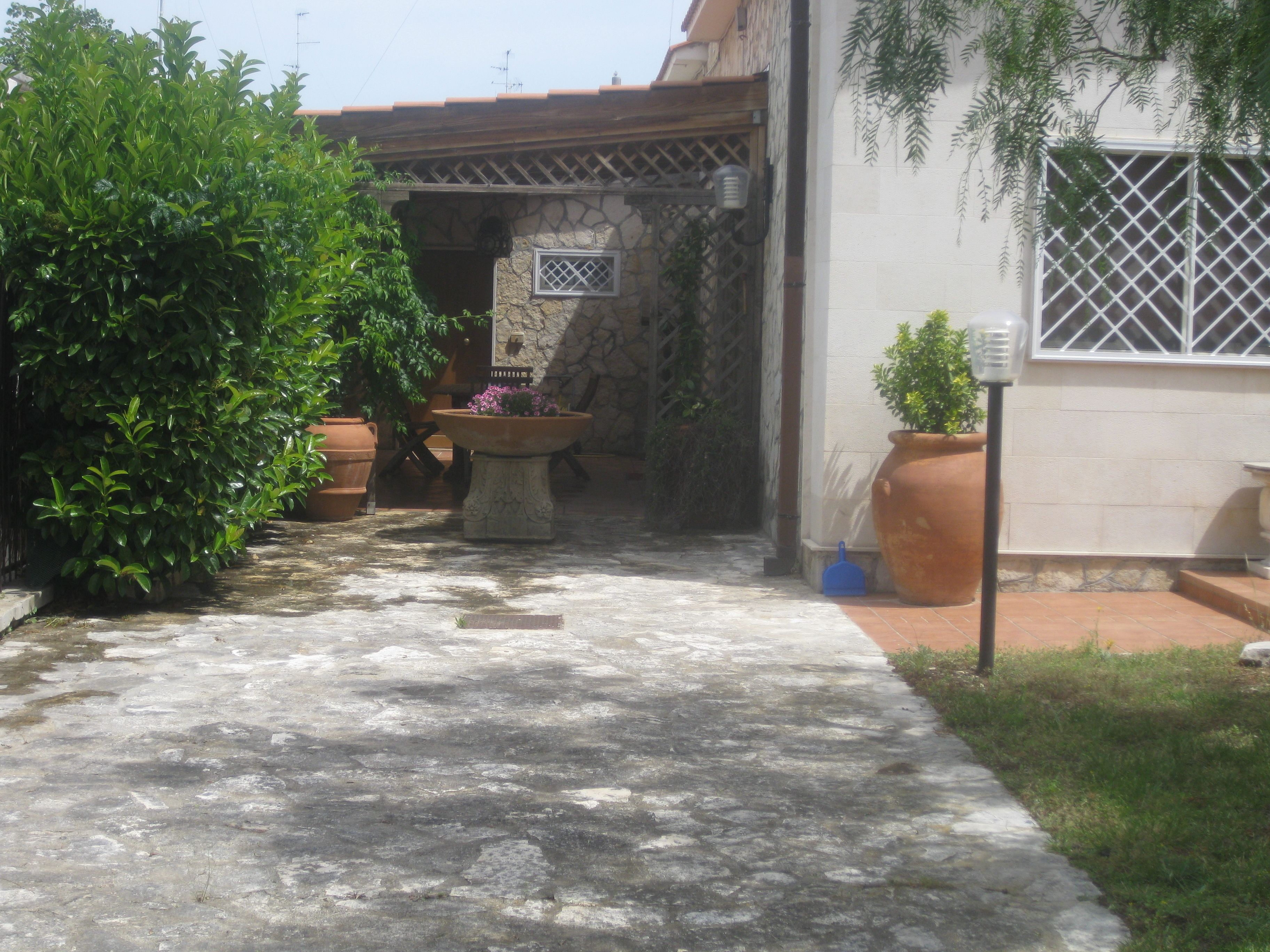 A courtyard with a stone floor, potted plants, and a stone wall.