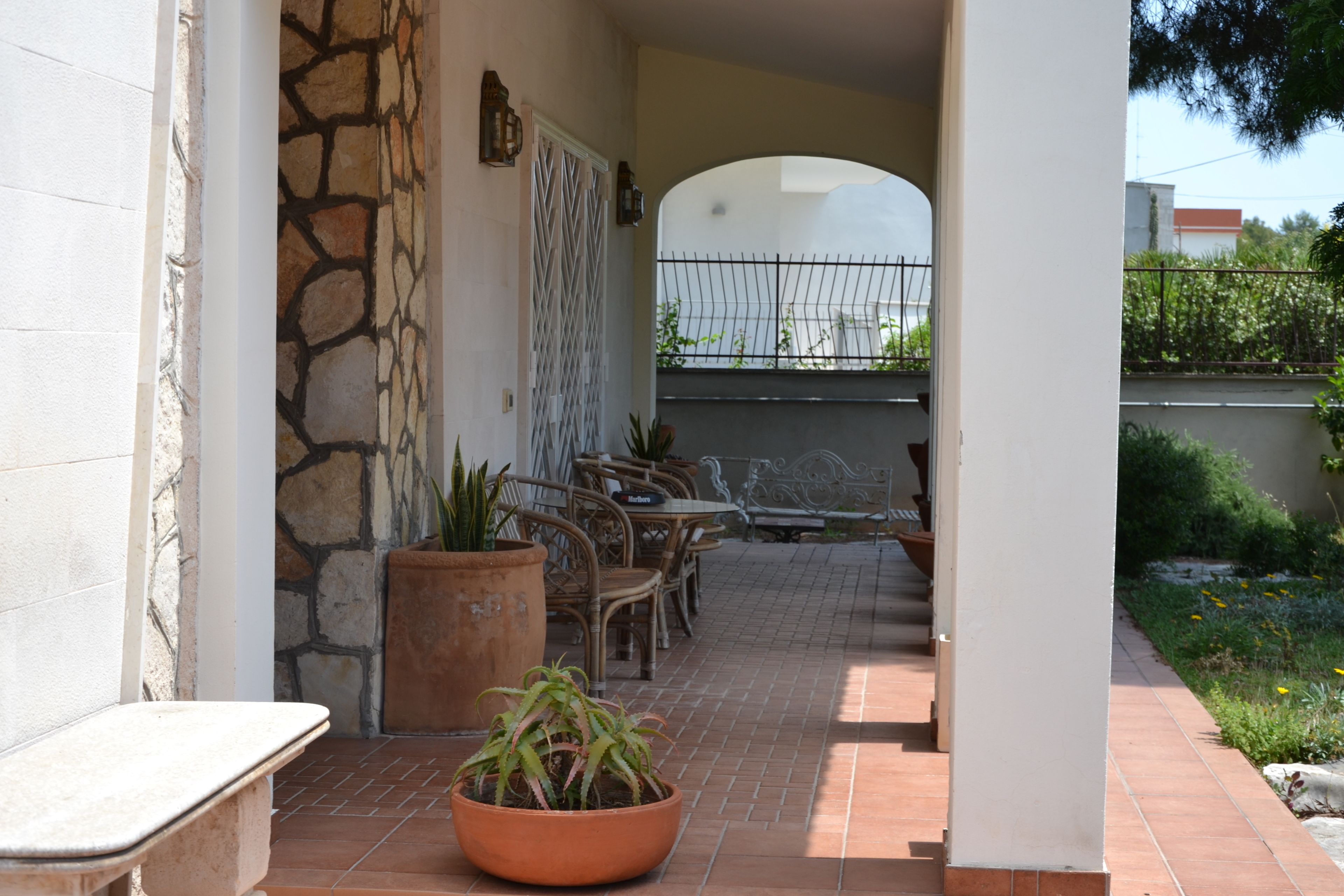 A covered patio area with a stone wall, a potted plant, outdoor furniture, and a view of the street.