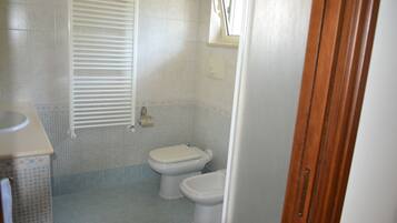 Uma casa de banho com duas sanitas, uma pia e uma janela.