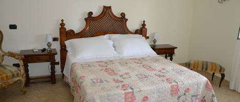 A bed with a floral quilt, wooden headboard, bedside tables with lamps, a chair, and a bench.