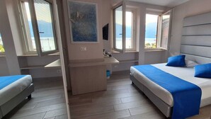 Ein Schlafzimmer mit zwei Betten, einem kleinen Schreibtisch und einem Fenster mit Meerblick.