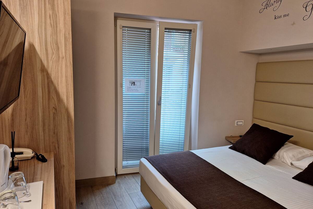 Ein Schlafzimmer mit einem Bett, einem Nachttisch, einem Spiegel und einem Fenster mit Jalousien.