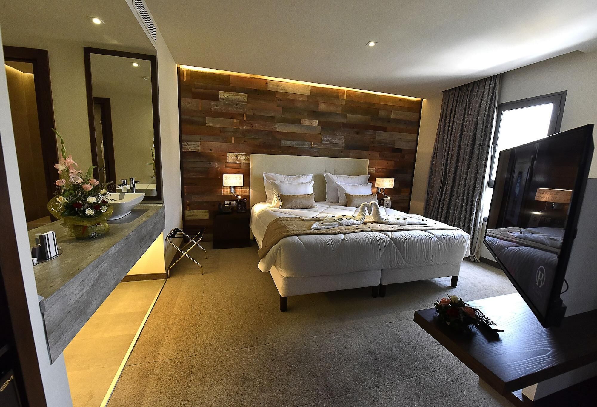 Une chambre d’hôtel avec un grand lit, des lampes de chevet, une télévision, un miroir et un mur décoratif en bois.
