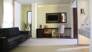 A modern living room with a black sofa, a small desk, a TV, and a bathroom with a sink and mirror.