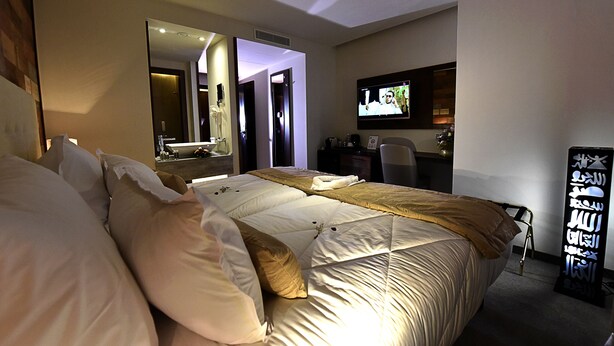 A hotel room with a large bed, a television, a desk, and a mirror.