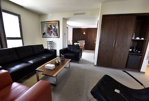 A modern living room with a black sofa, a wooden coffee table, and a dining area with a table and chairs.