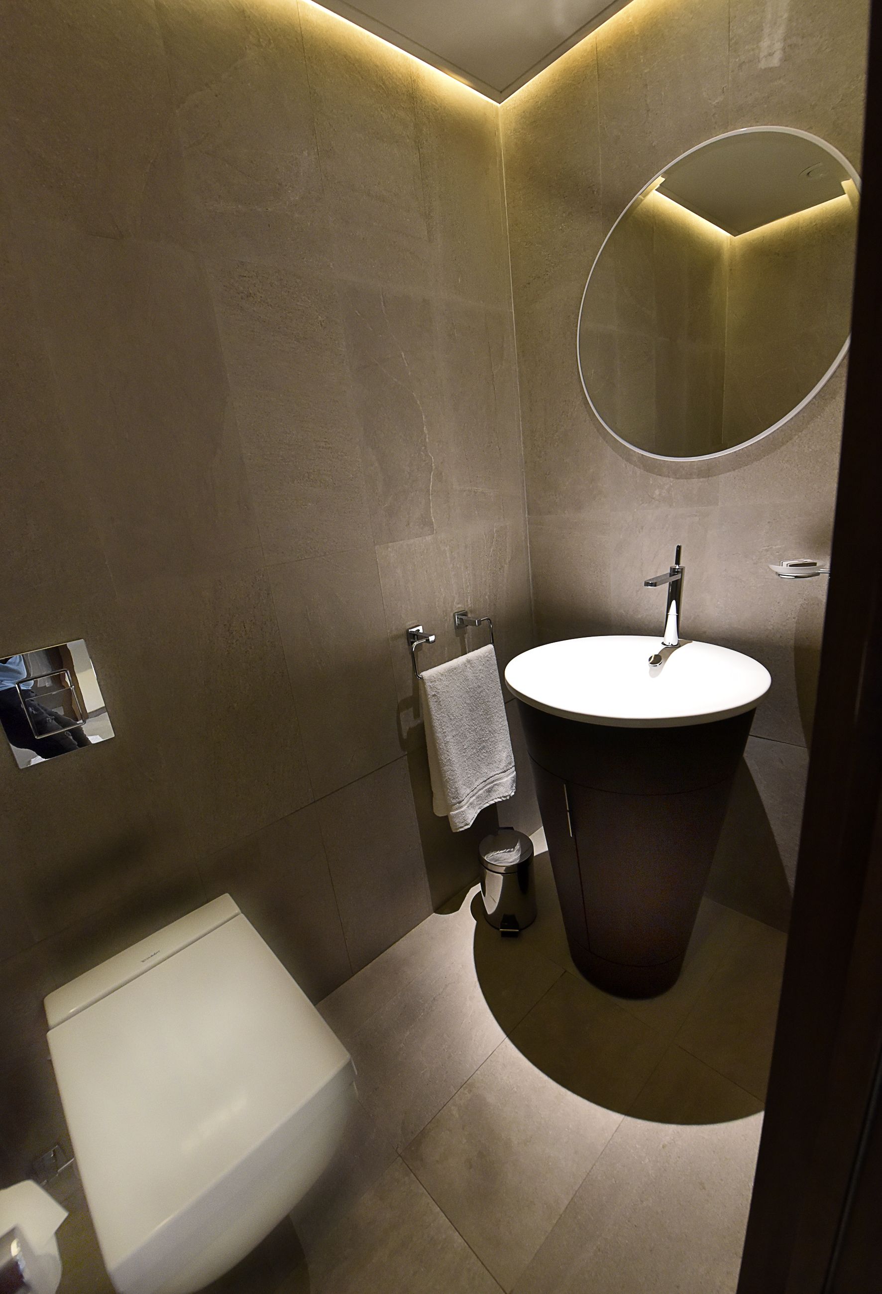 A modern bathroom with a round mirror, a pedestal sink, and a toilet.